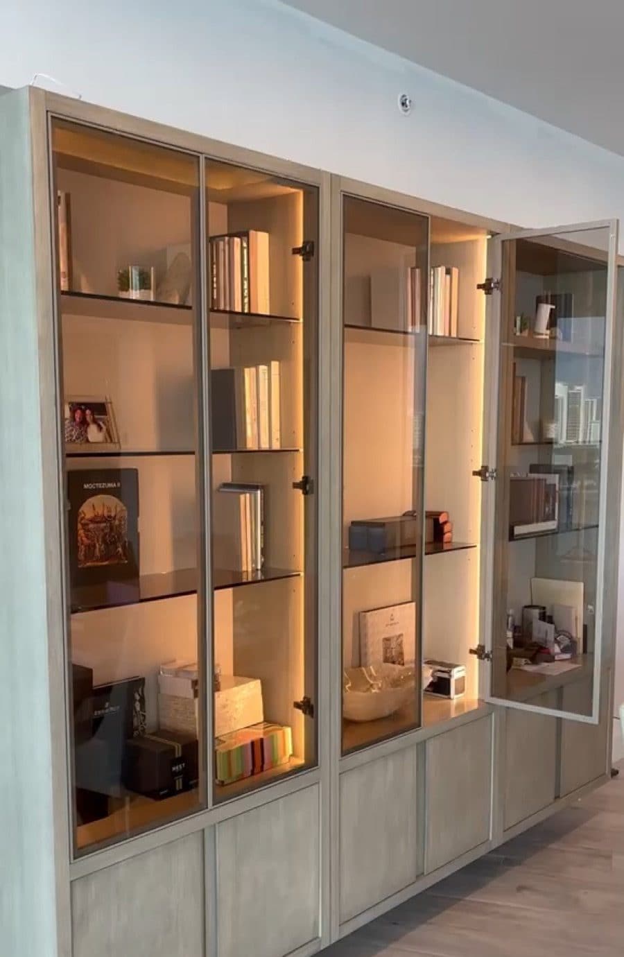 Built-in display wall with aluminum-framed glass doors, smoked glass shelves and warm integrated lighting
