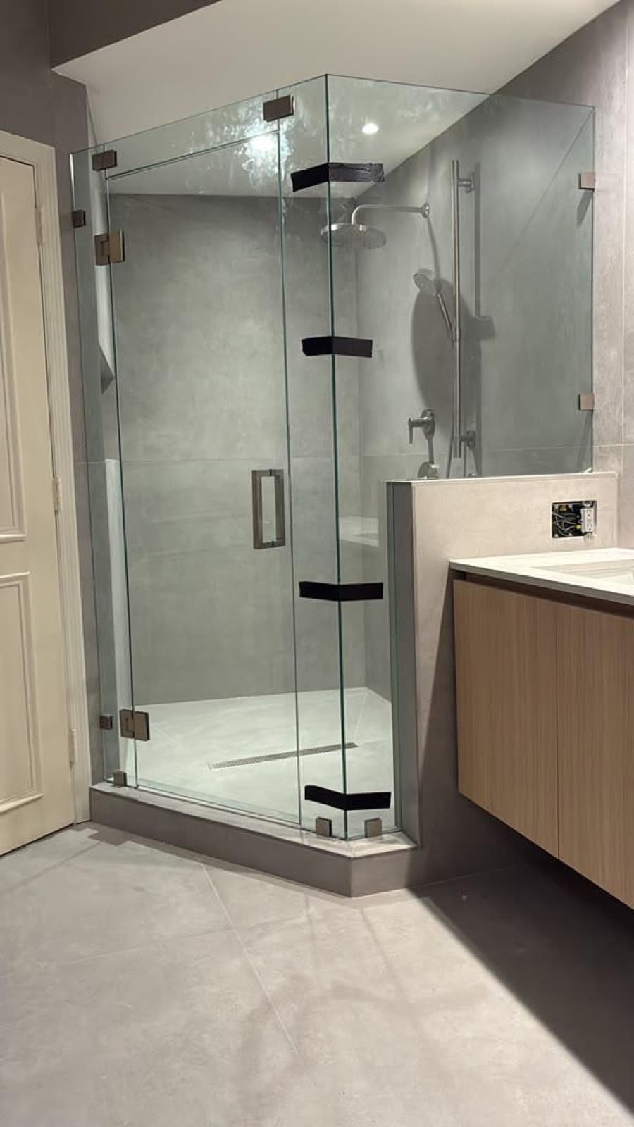 Frameless glass shower enclosure with precision hinges beside a floating wood vanity